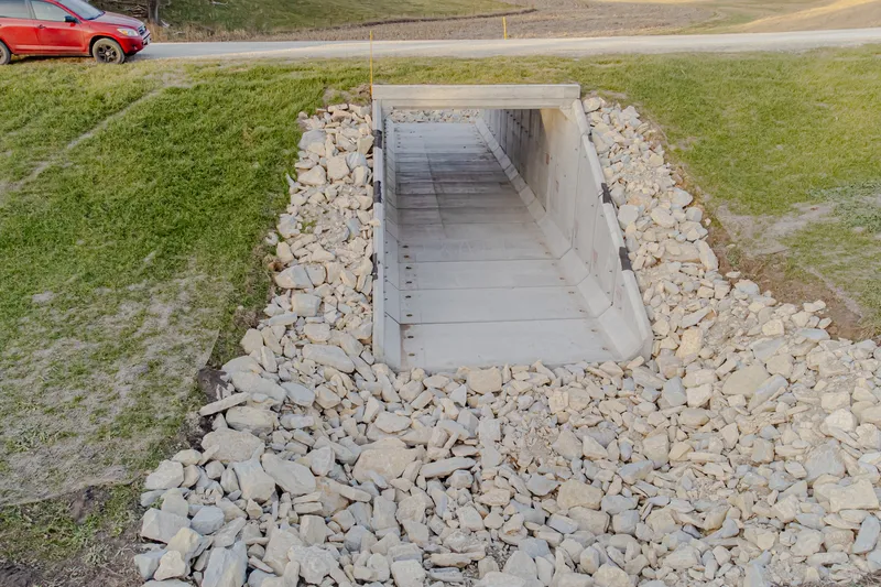 Konstruksi gorong-gorong box culvert beton pracetak dan sayap wingwall penahan erosi riprap batu belah di bawah badan jalan lingkungan desa